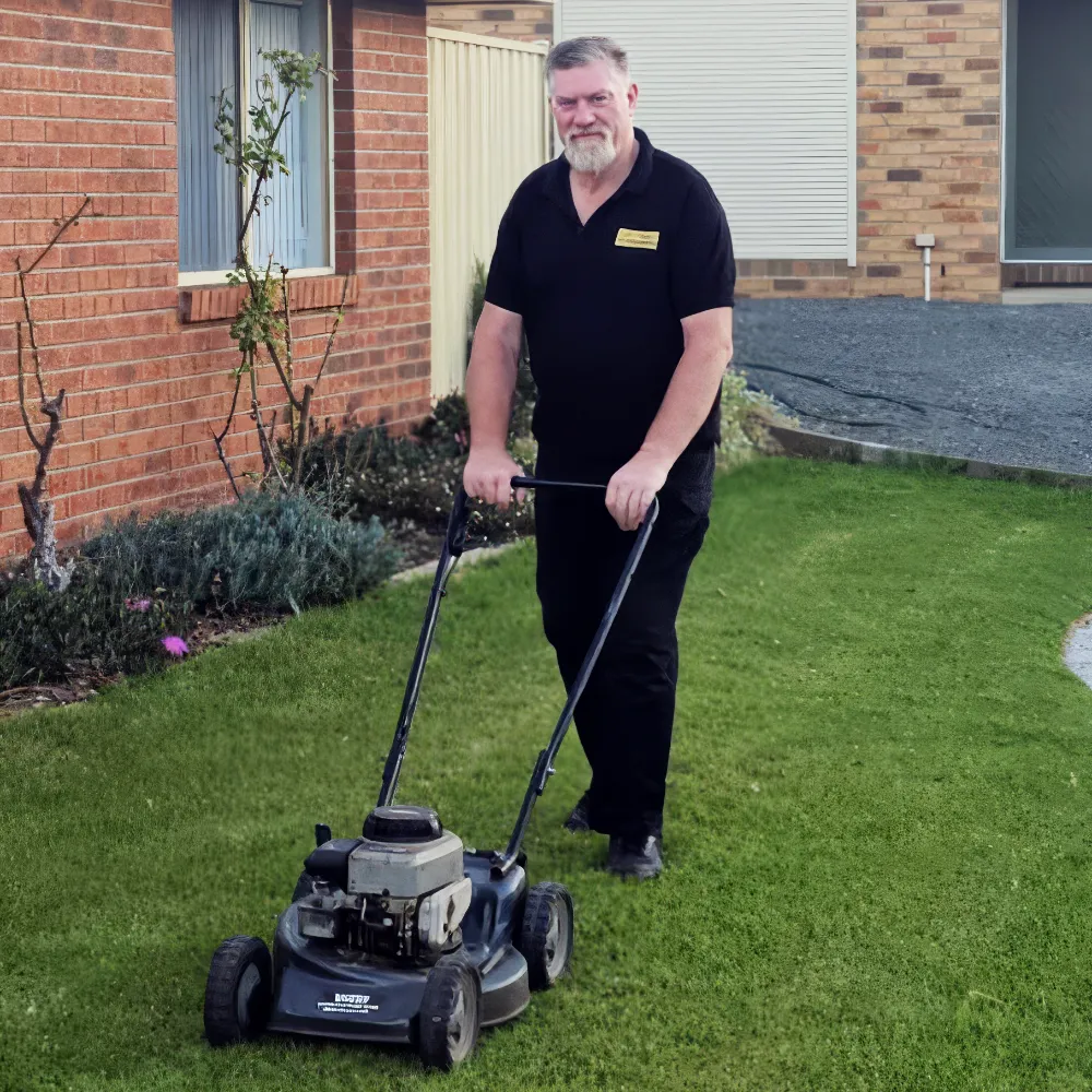 An action image of Marc mowing a lawn against a background ground of a redbrick house, tidy flower beds and a paved driveway.